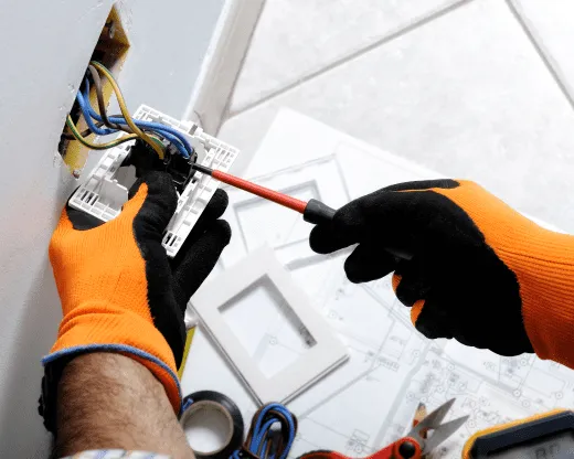 Un électricien en gants orange travaille sur un mur.