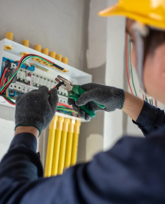 Un homme en casque et gants travaillant sur un panneau électrique pour l'installation de systèmes électriques.