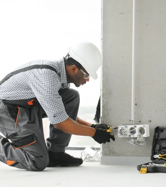 Un homme en salopette et casque de sécurité travaillant sur des équipements électriques pour l'installation de systèmes électriques.