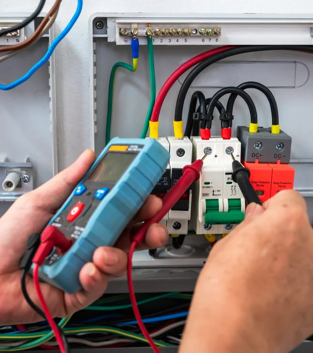 Une personne utilise un multimètre pour vérifier le câblage électrique lors de l'installation de systèmes électriques.