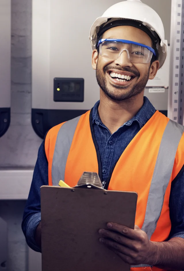 Un homme en gilet orange et lunettes de sécurité tenant un clipboard, travaillant sur l'installation de systèmes électriques.